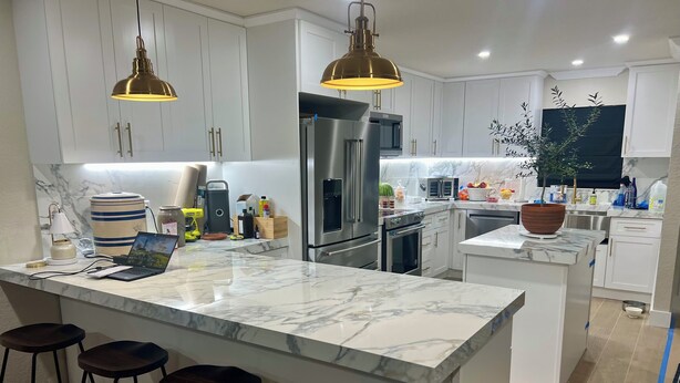 A modern kitchen with white cabinets, a marble island, and stainless steel appliances. There are bar stools and a potted plant. - Be one of the first guests to enjoy this newly renovated luxury waterfront villa (Punta Gorda)