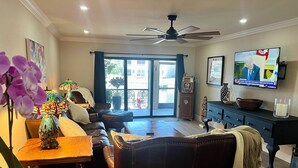 A living room with a sofa, coffee table, and TV. There is a window with curtains, a ceiling fan, and a decorative lamp. - Be one of the first guests to enjoy this newly renovated luxury waterfront villa (Punta Gorda)
