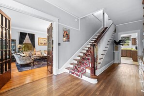A staircase with a red carpet, a wooden floor, a sofa, a chair, and a bookshelf.