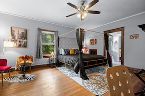 A bedroom with a four-poster bed, a ceiling fan, a window with curtains, a red chair, a zebra rug, and a wooden chair.