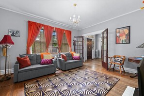 A living room with two grey sofas, a patterned rug, a chandelier, and a wooden chair.