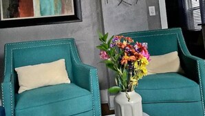 Twee smaragdgroene fauteuils met witte kussens en een vaas met kleurrijke bloemen op een witte tafel.