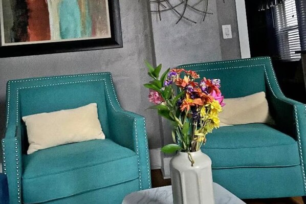 Two teal armchairs with white cushions and a vase of colorful flowers on a white table.