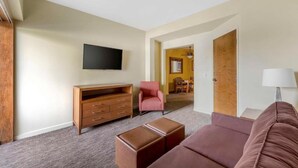 Una sala de estar con una televisión de pantalla plana, un mueble de madera, un sillón rosa, un reposapiés marrón y un sofá.