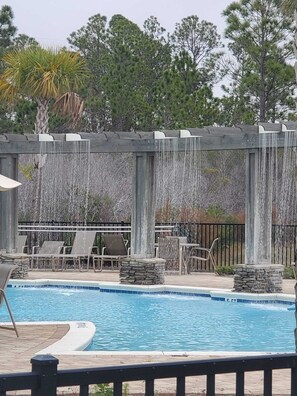 Zona de piscina con sillones de descanso y una pérgola con luces colgantes.