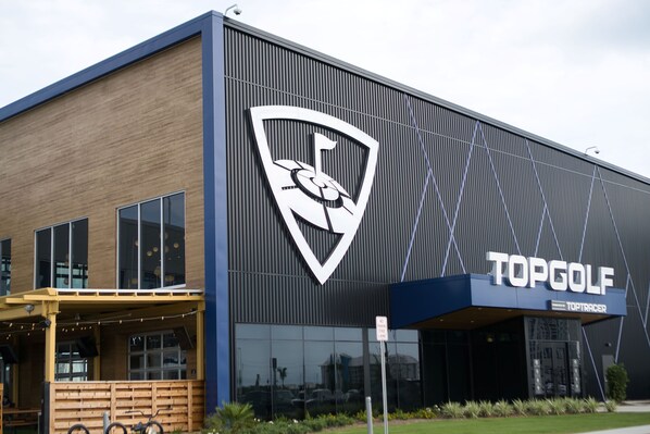 Un edificio moderno con un gran logotipo y el nombre "TOPGOLF" en la fachada.