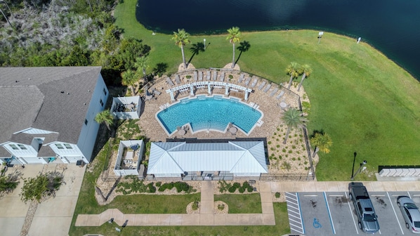 Vista aérea de un resort con piscina, sillas de descanso y palmeras.