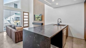 Une cuisine moderne dotée d’un grand îlot central, d’un téléviseur encastré et offrant une vue sur un quartier résidentiel.