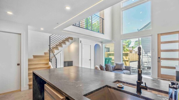 Une cuisine spacieuse dotée d’un grand îlot central, d’un escalier et offrant une vue sur l’extérieur.