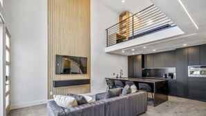 Un intérieur moderne avec un canapé gris, une cuisine dotée de meubles sombres et un escalier menant à un niveau supérieur.