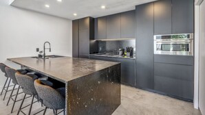 Une cuisine moderne dotée d’un grand îlot central, de tabourets de bar et d’appareils électroménagers intégrés.