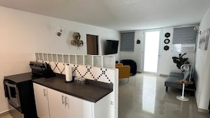 Una cocina moderna con encimera negra, armarios blancos y salpicadero de azulejos. Hay un comedor con sofá y mesa de centro.