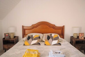 Een netjes opgemaakt bed met gestreepte kussens, een houten hoofdbord en twee nachtkastjes met lampen en decoratieve objecten.