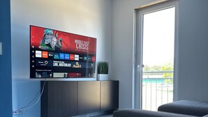 Una sala moderna con un televisor de pantalla plana montado en la pared, un sofá gris, una mesita con un control remoto y una planta en maceta.