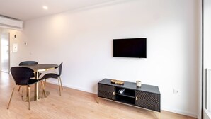 Ein modernes Wohnzimmer mit einem runden Esstisch, schwarzen Stühlen, einer schwarzen Unterhaltungsecke und einem Wand-Fernseher.