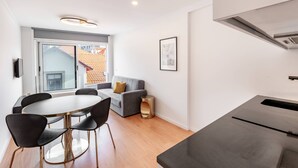 Ein modernes Wohnzimmer mit einem grauen Sofa, einem runden Esstisch mit Stühlen und einem großen Fenster mit Blick auf Gebäude.