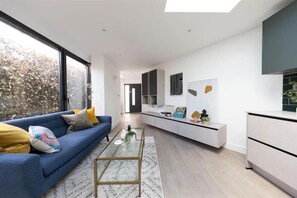 Un salón moderno con un sofá azul, una mesa de centro de cristal y vistas al exterior a través de amplios ventanales.