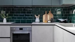 Une cuisine moderne avec des meubles gris, un four noir et un pare-feu vert.