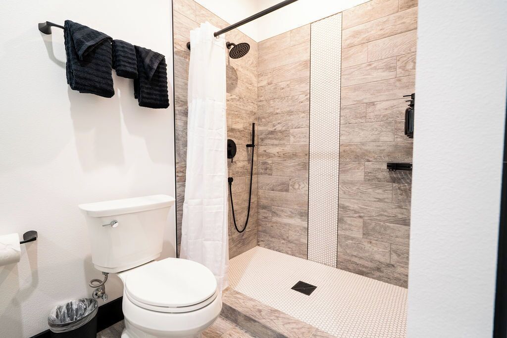 Een moderne badkamer met toilet, douche en een handdoekrek met handdoeken.