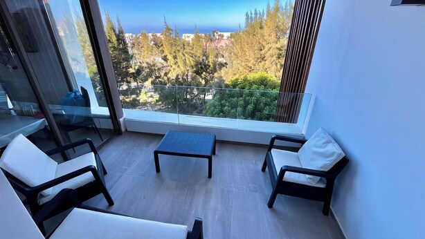A balcony with a view of trees and a distant landscape. There are two white chairs and a small table. - Cosy and chic one-bedroom apt with 3 beds - Taghazout Bay (Sidi Bouzid)
