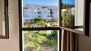 A room with a large window offering a view of a modern building and a landscaped garden. - Cosy and chic one-bedroom apt with 3 beds - Taghazout Bay (Sidi Bouzid)