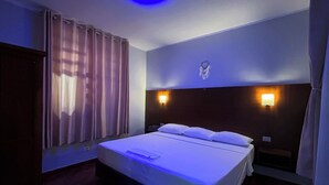 Habitación de hotel con cama, cortinas, cabecera con luces de pared y luz de techo.