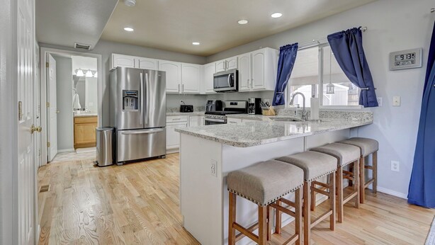 A modern kitchen with white cabinets, stainless steel appliances, and a central island with bar stools. - Front Range Getaway - 4 beds with Jacuzzi (Colorado Springs)