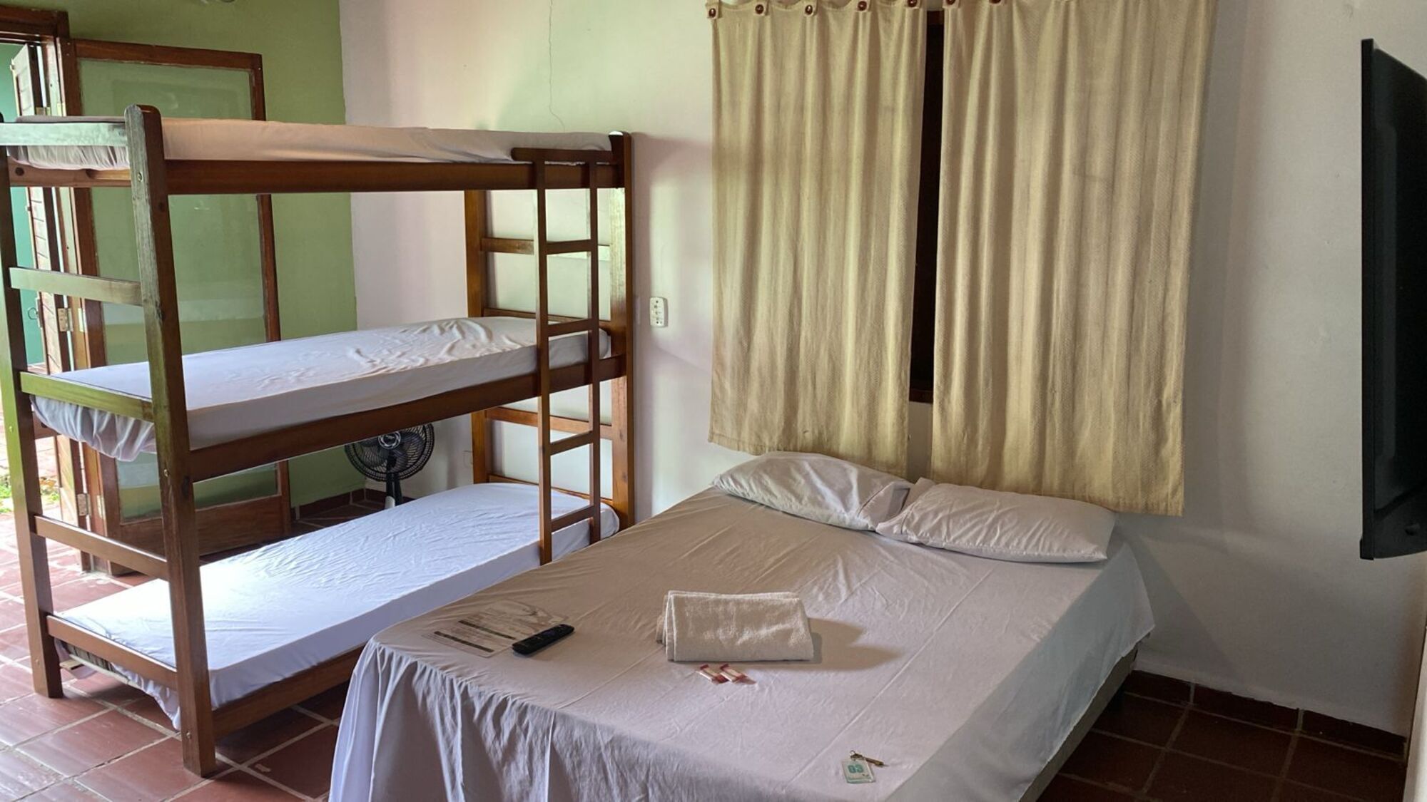 A room with a bunk bed, a single bed, a fan, and a TV.