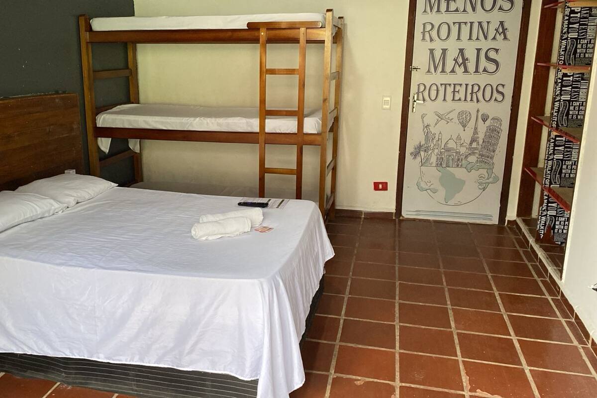 Un lit simple, avec un lit superposé en bois adossé au mur, une literie blanche et une affiche illustrant des thèmes liés au voyage.