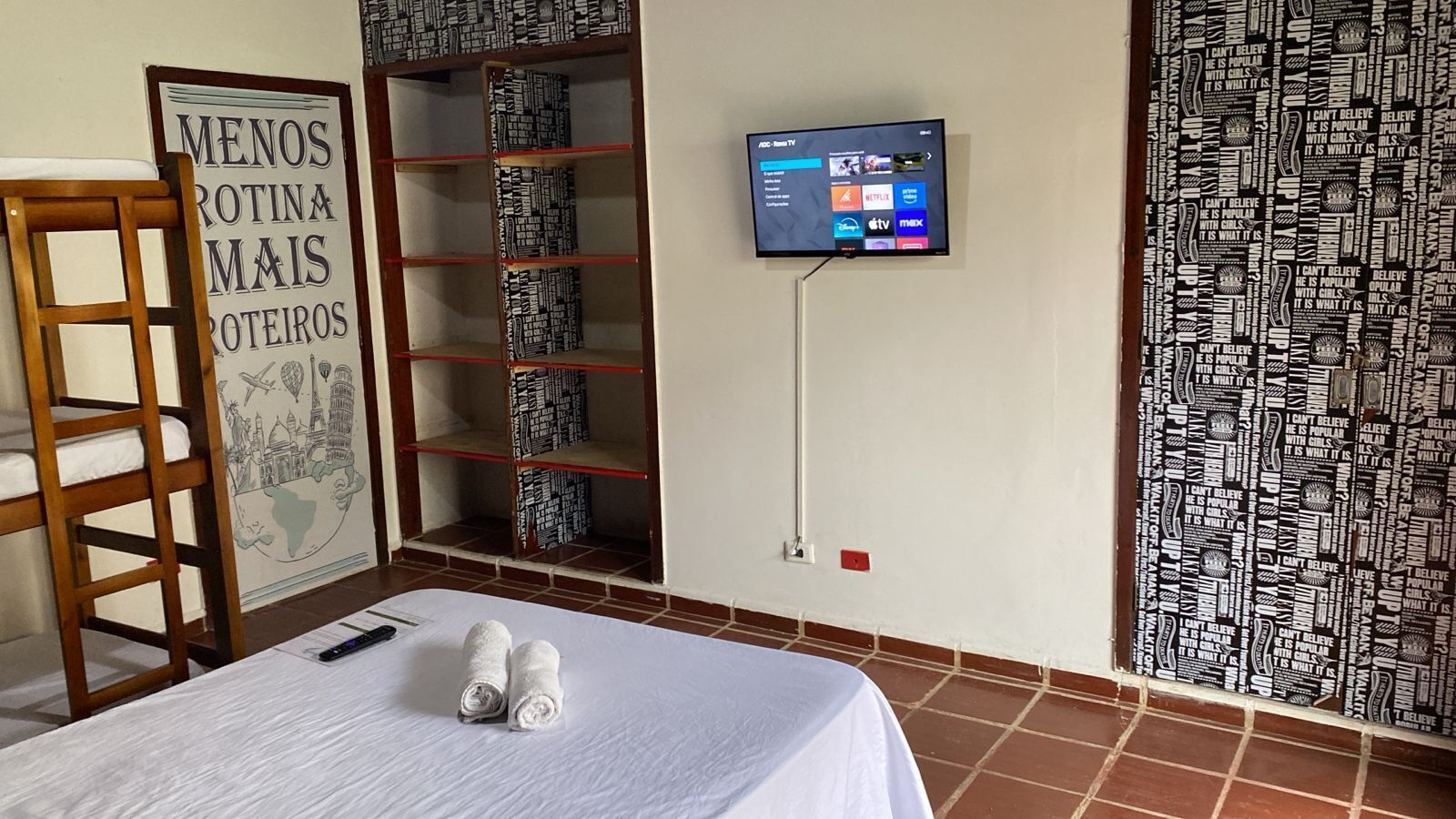 Habitación de hotel con cama, televisor montado en la pared, estantería y un cartel en la pared.
