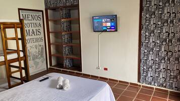 Habitación de hotel con cama, televisor montado en la pared, estantería y un cartel en la pared.