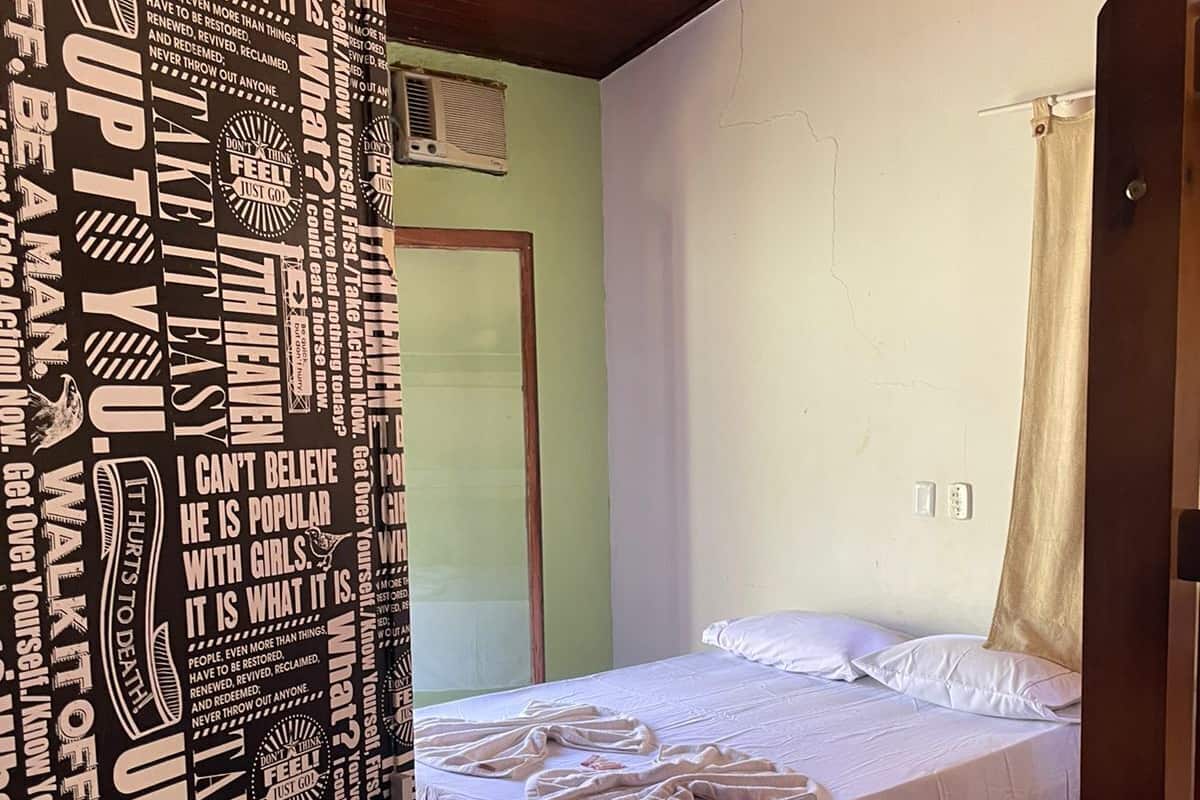 Une chambre à coucher avec un lit, un ventilateur de plafond, une fenêtre avec des rideaux et une porte.
