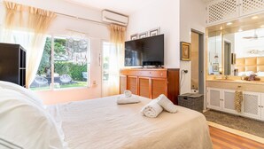 Ein Hotelzimmer mit Bett, Fernseher, Badezimmer mit Spiegel und Waschbecken sowie Blick ins Freie.