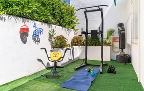 A small outdoor workout area with a pull-up bar, a bench, a yoga mat, and a punching bag.