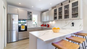 Eine moderne Küche mit einem Edelstahl-Kühlschrank, einer Marmorarbeitsplatte und hölzernen Barhocker.