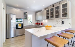 A modern kitchen with a stainless steel refrigerator, a marble countertop, and wooden bar stools.