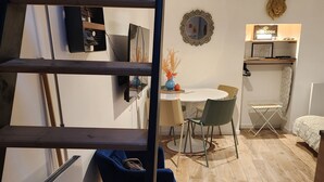 A modern interior with a wooden staircase, a dining area with a white table and chairs, and a small kitchen area with a map and a framed picture on the wall. - The wash house (Ballan-Miré)