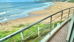 A balcony with a view of a beach, a railing, and a tiled floor.
