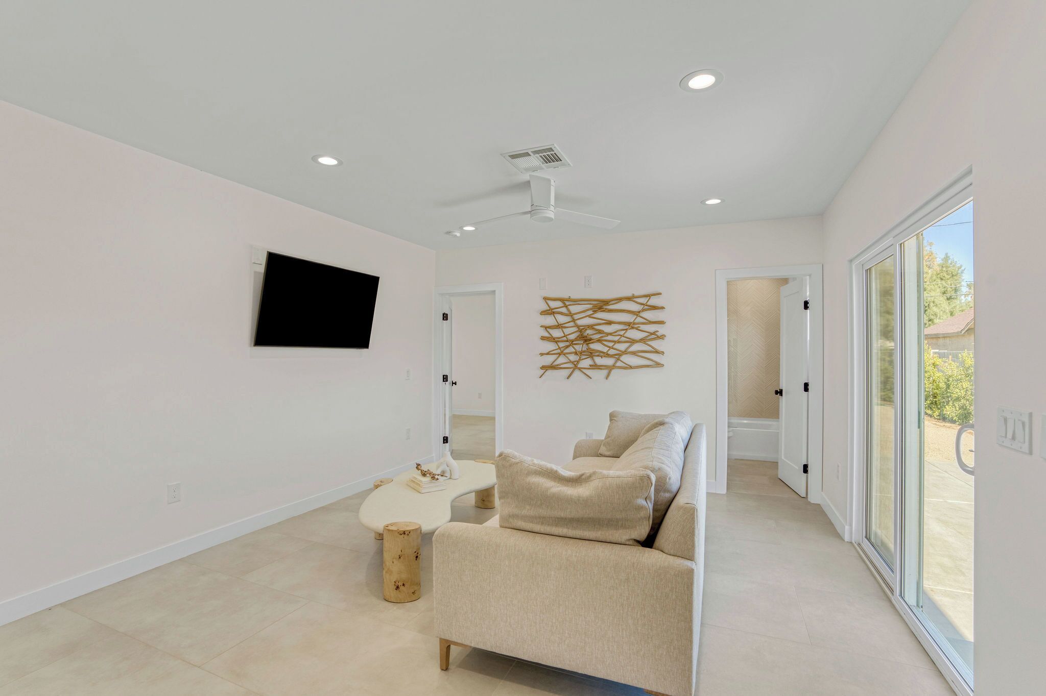 A modern living room with a beige sofa, a white coffee table, and a mounted flat-screen TV.