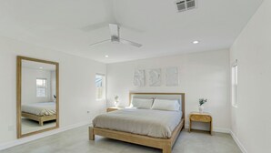 Une chambre à coucher comprenant un lit, un ventilateur de plafond, un grand miroir, des tables de chevet et des œuvres d’art accrochées au mur.