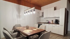 A modern kitchen with white cabinets, a wooden ceiling, and a dining area with a wooden table and chairs. - Vacation apartment 1 at Steinhuder Meer - near 'Alte Moorhütte'  (Neustadt am Rübenberge)