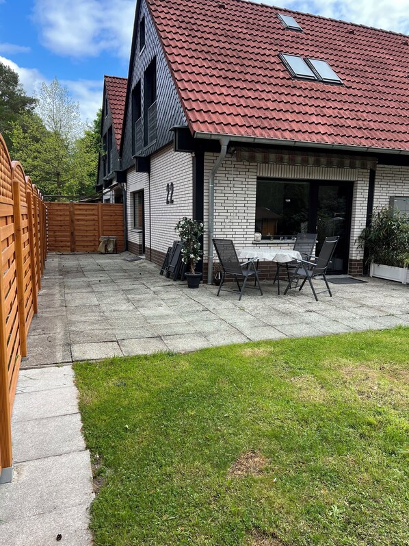 Et toetagers hus med rødløvet tag, murstensfacade og en patio med bord og stole.
