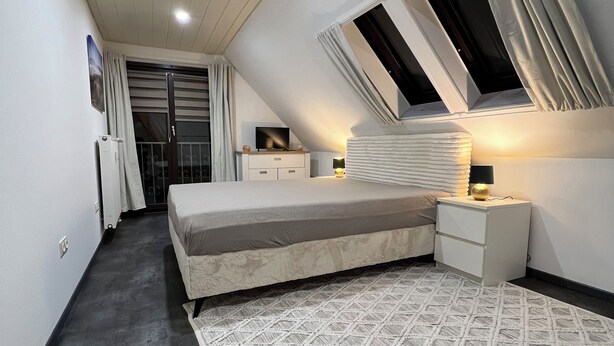 A bedroom with a bed, a nightstand, a TV, and a window with curtains. - Vacation apartment 1 at Steinhuder Meer - near 'Alte Moorhütte'  (Neustadt am Rübenberge)