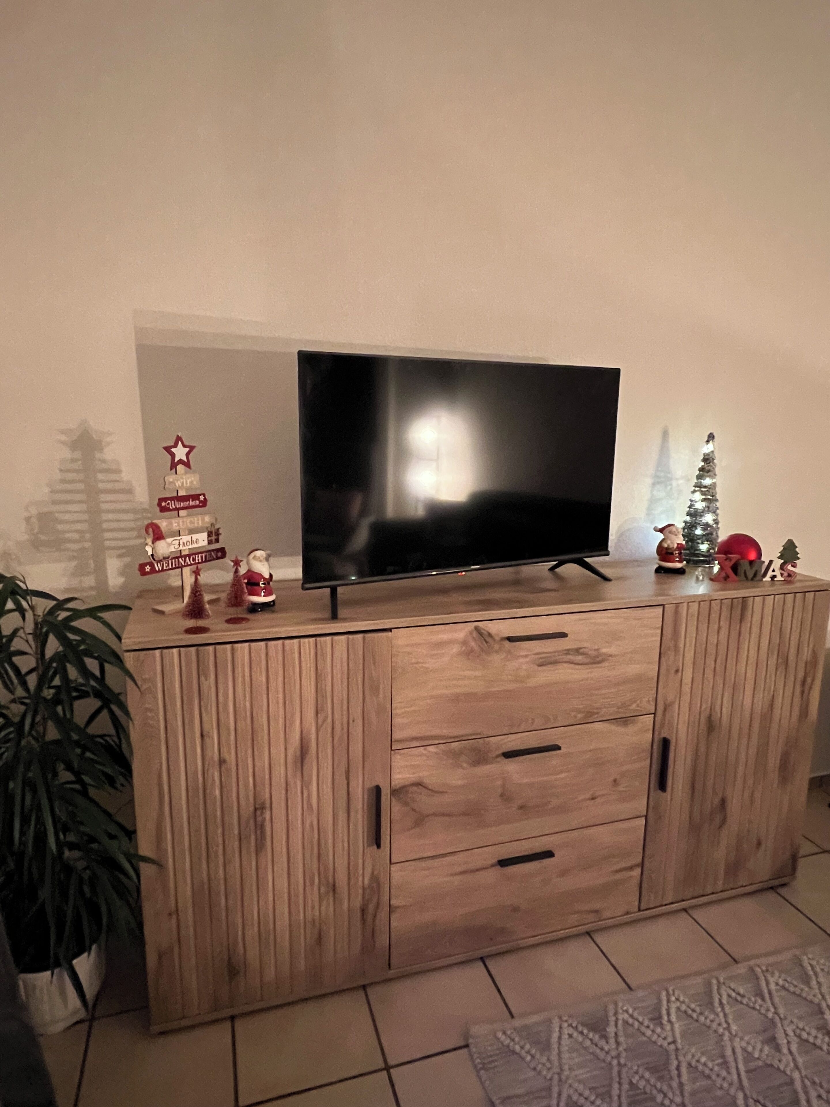 A wooden TV stand with a flat-screen TV, Christmas decorations, and a potted plant.
