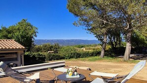 Un espace extérieur aménagé avec une table et des chaises, une bouteille et un verre posés sur la table.