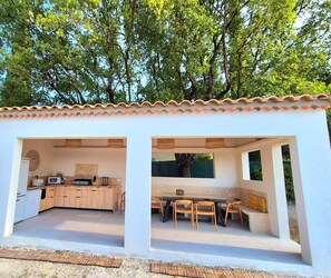 A compact outdoor kitchen with a dining area, surrounded by a white wall and a tiled roof. - Villa L'Estef: A Relaxing Summer by the Pool—Beautiful Views, Relaxation, and Fun, Right in the Heart of the Village! (Alleins)