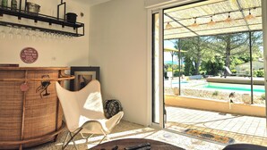 Une pièce comprenant un coin bar, une chaise, une table et donnant sur une piscine extérieure.