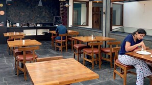Ένα εστιατόριο με ξύλινα τραπέζια και καρέκλες, δάπεδο με πέτρινα πλακάκια και φωτιστικά οροφής.