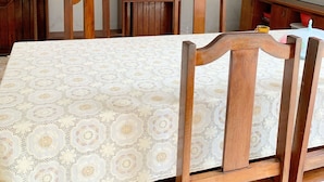 A dining area with a table covered in a patterned tablecloth, surrounded by wooden chairs and a wooden cabinet with shelves. - Pousada Estilo Brasil (Fortaleza)