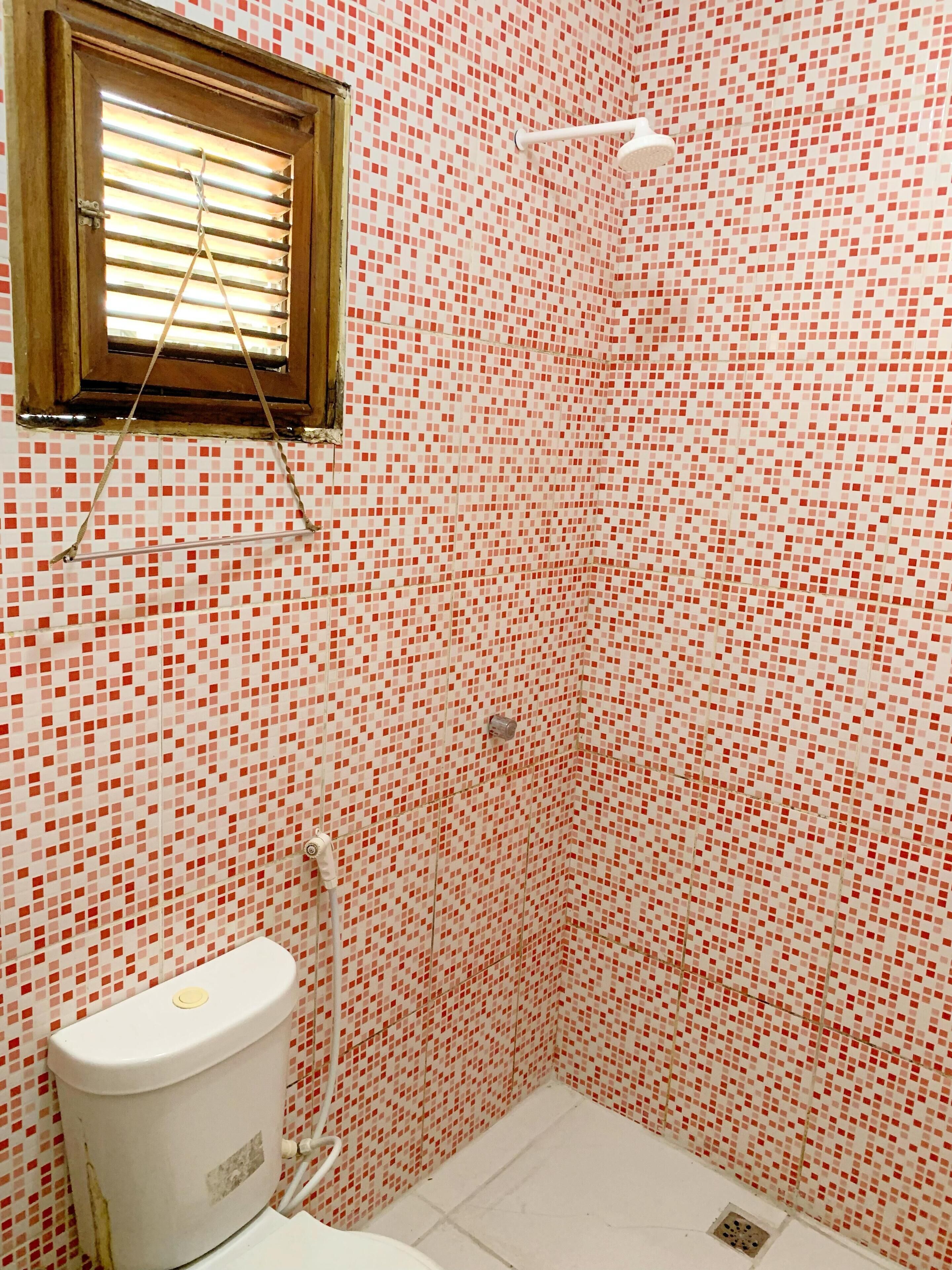 A bathroom with a toilet, a shower, and a window with blinds.